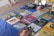 A collection of vintage vinyl records is displayed on a blue cloth. Various album covers with colorful artwork and text are visible, reflecting a range of music genres. There are also some cassette tapes and other miscellaneous items on the table. The setting appears to be an outdoor market, with a tiled surface visible underneath.