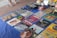 A collection of vintage vinyl records is displayed on a blue cloth. Various album covers with colorful artwork and text are visible, reflecting a range of music genres. There are also some cassette tapes and other miscellaneous items on the table. The setting appears to be an outdoor market, with a tiled surface visible underneath.