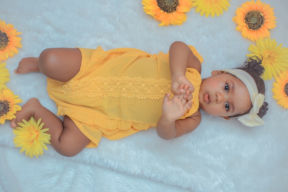 baby in yellow dress lying on white textile