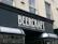 A storefront sign with the text 'BeerCraft of Bath' displayed in bold letters on a dark facade. The building is light-colored stone with two windows above the sign and a security camera mounted beside one window.