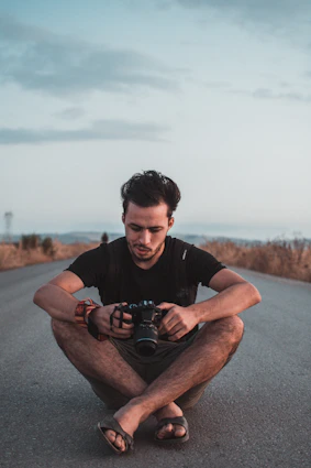 man sitting on road holding DSLR camera