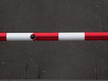 A horizontal barrier arm with red and white stripes is positioned across a flat, dark gray concrete surface.
