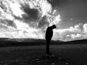 A silhouette of a lone figure standing against a vast, empty horizon under a cloudy sky.