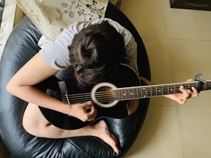 person playing guitar while sitting on lather bean bag chair