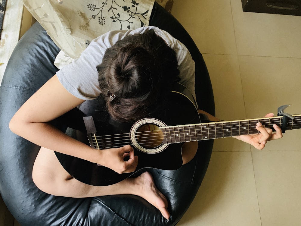person playing guitar while sitting on lather bean bag chair