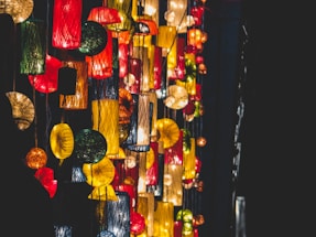 Brightly colored hanging lanterns with varied shapes and sizes create an artistic and festive atmosphere. The lanterns emit warm light, contrasting with the dark background.