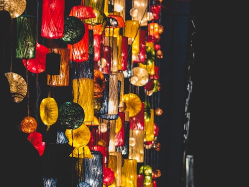 Brightly colored hanging lanterns with varied shapes and sizes create an artistic and festive atmosphere. The lanterns emit warm light, contrasting with the dark background.
