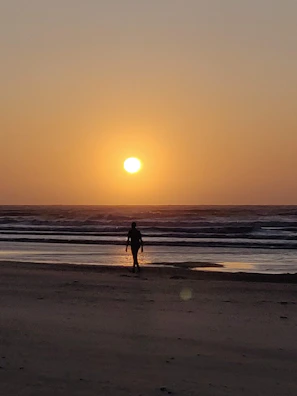 A serene beach scene with a male traveler walking along the shoreline under a sunset sky.