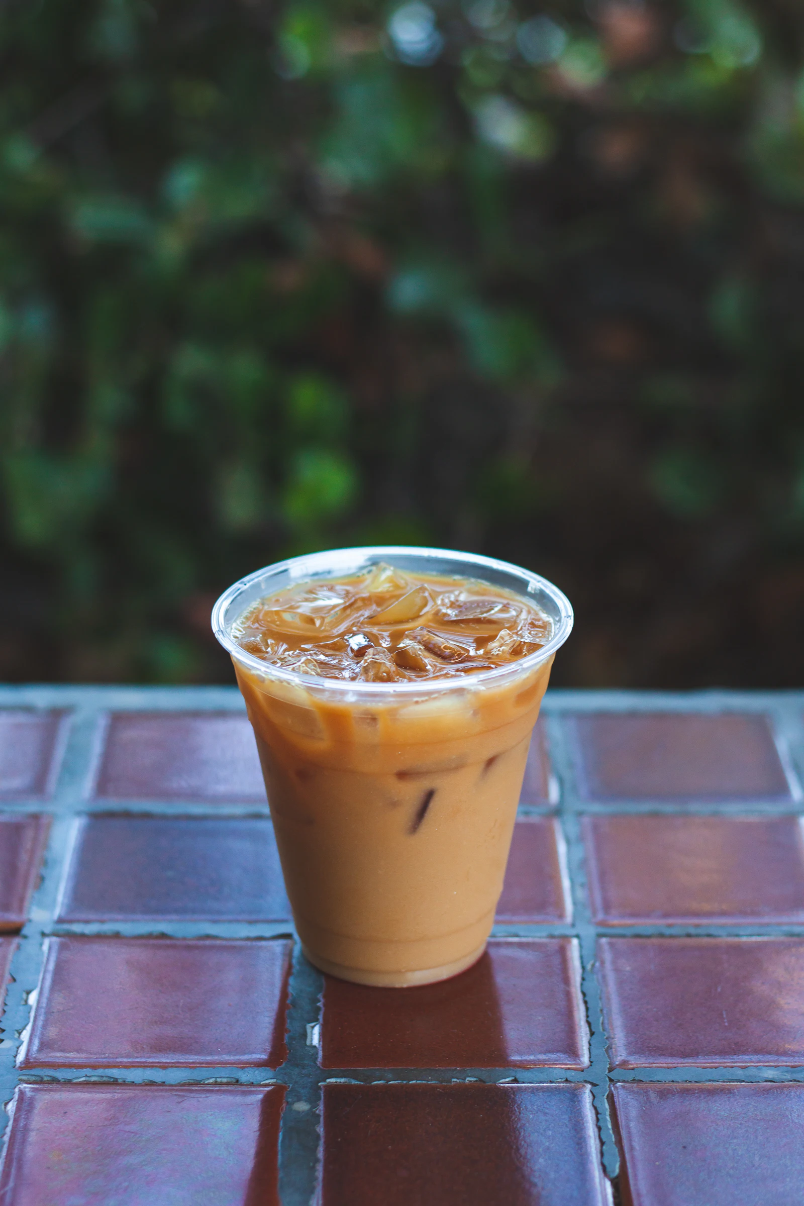 A clear cup of iced milk tea on a tiled table with green leaves behind it