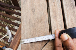 Close-up of hands measuring wood beams with a tape measure on a construction site.