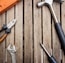 A collection of hand tools arranged on a wooden surface, including a hammer with a black handle, pliers with orange grips, an adjustable wrench, and a screwdriver.
