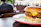 A cheerful man savoring a gourmet burger at an outdoor urban eatery with city skyline in the background.