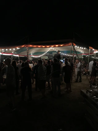A bright, spacious event tent set up outdoors with people enjoying a festive gathering under string lights.