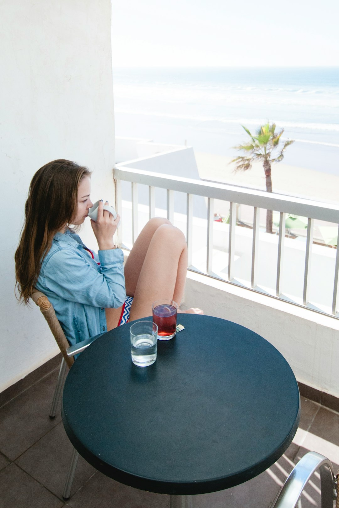 woman wearing teal dress shirt sitting on brown chair while looking at seashore