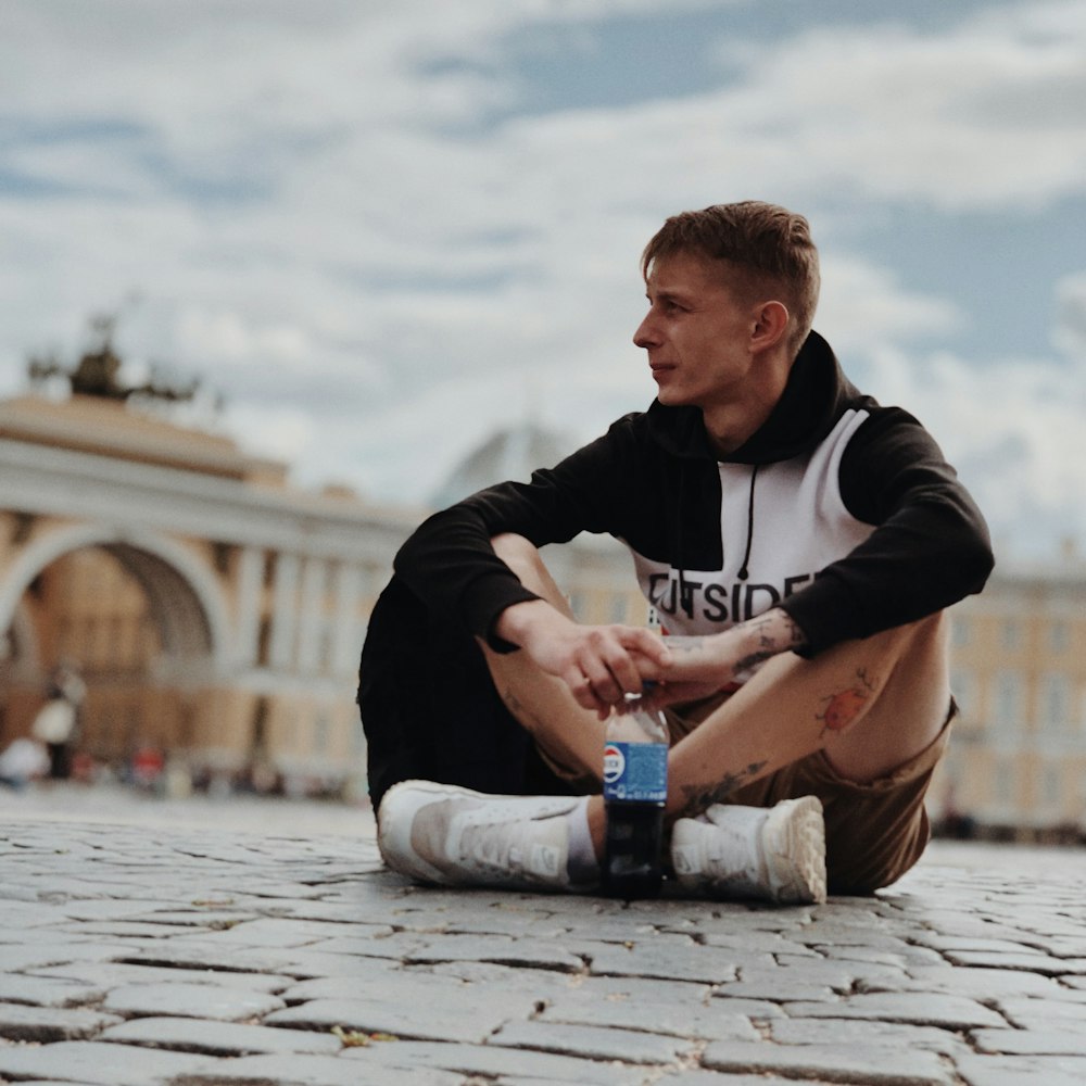 man sitting on ground while holding Pepsi bottle