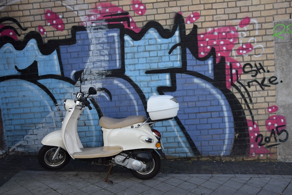 white motor scooter parked besides multicolored wall with graffiti