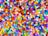 A multitude of small, colorful plastic beads scattered in a chaotic pattern. The beads are cylindrical in shape and appear in a wide array of vibrant colors including red, blue, green, yellow, purple, and more.