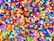 A multitude of small, colorful plastic beads scattered in a chaotic pattern. The beads are cylindrical in shape and appear in a wide array of vibrant colors including red, blue, green, yellow, purple, and more.