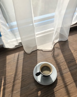 Soft morning light filtering through a sheer curtain onto a simple ceramic coffee cup on a wooden table.