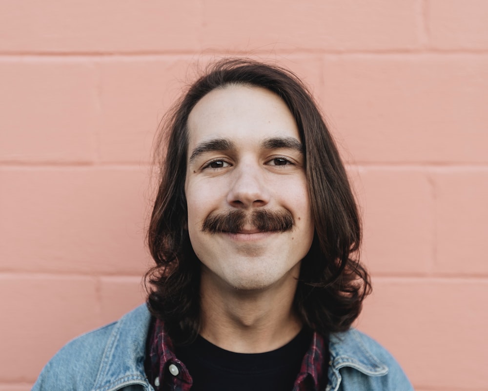 smiling man in blue denim jacket in front of wall