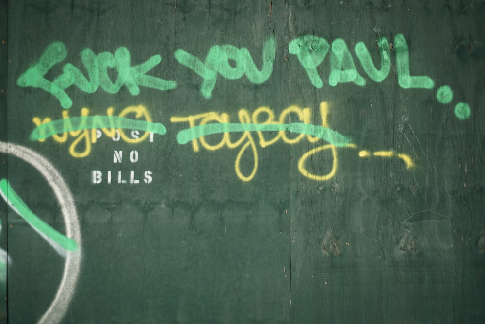 a green wall with graffiti written on it