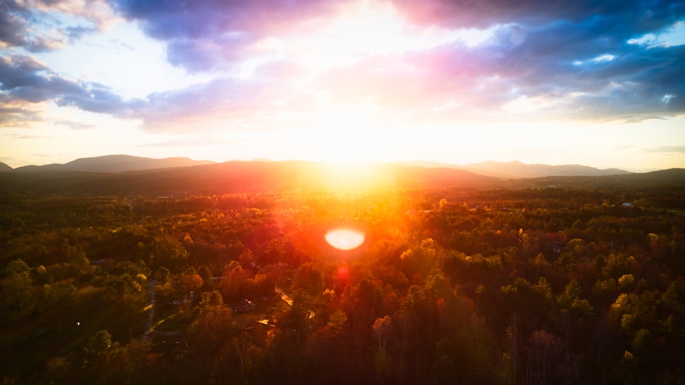 the sun is setting over a forest with mountains in the background