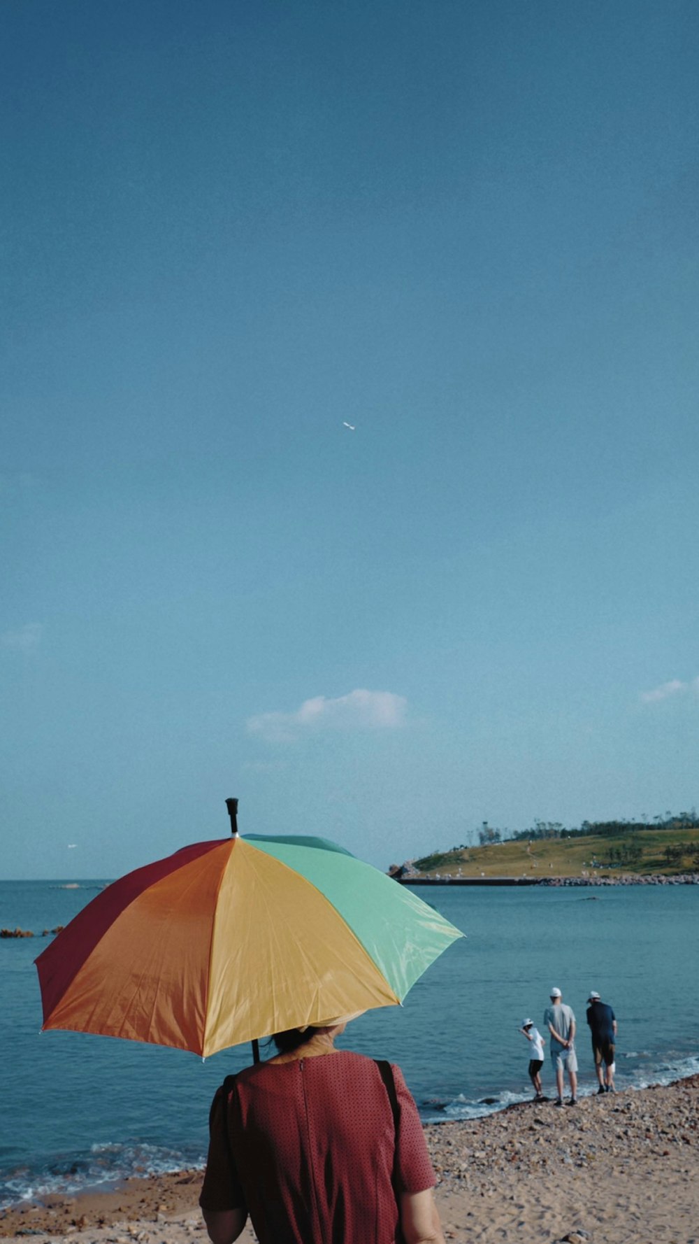 Foto persona sosteniendo un paraguas multicolor frente al cuerpo de agua –  Imagen 山东省中国 gratis en Unsplash