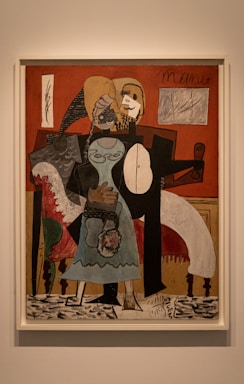 A painting featuring abstract human figures with geometric forms and distorted features. The background includes a red wall, light-colored frame, and elements suggestive of furniture. The figures are rendered in contrasting shades, with black, white, and various earthy tones. The style is reminiscent of cubism, characterized by fragmented shapes and overlapping planes.