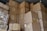A large stack of brown cardboard boxes piled up in a storage area. The boxes are sealed with tape and have various labels and shipping details attached. The ceiling and a small surveillance camera are visible above the stacked boxes.