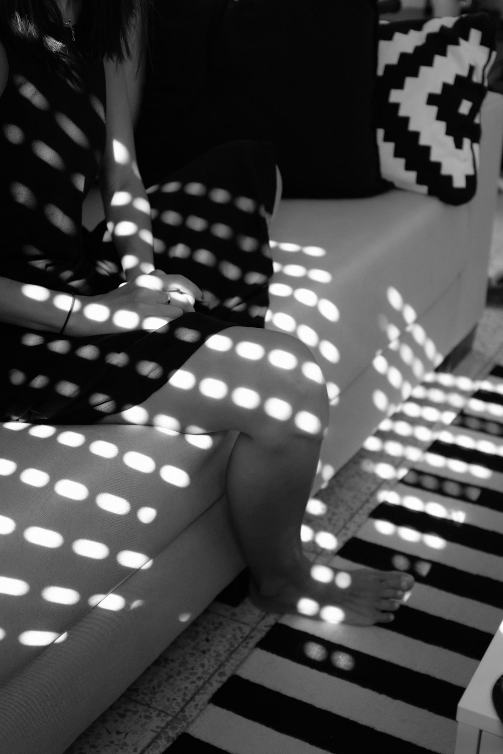 Photographie en niveaux de gris d’une personne pieds nus assise sur un canapé