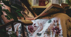 A cozy corner with botanical prints on the wall and a person reading a plant care book while sipping tea.