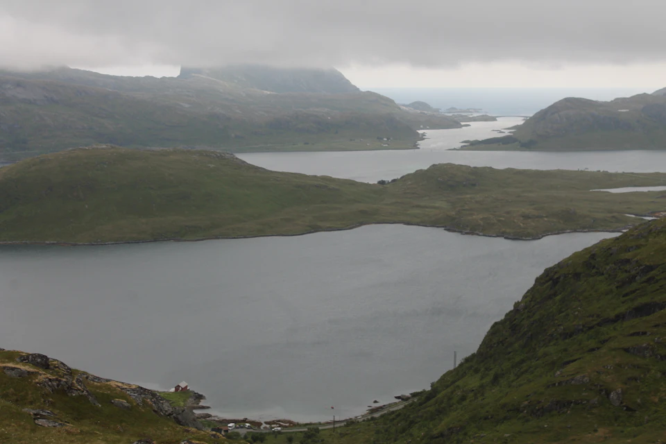 The image depicts a serene landscape with three large lakes nestled amidst lush green hills and mountains. The largest lake is situated on the left side, surrounded by smaller lakes that are evenly distributed across the scene. The sky above is overcast, casting a soft light over the entire landscape. In the foreground, there's a small village or town, adding a touch of human presence to this natural setting.