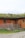Several sheep graze on a grassy roof of a wooden barn. The barn has a rustic appearance with a natural wood finish and small green-framed windows. There is a metal gate and some wooden crates near the barn.