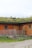 Several sheep graze on a grassy roof of a wooden barn. The barn has a rustic appearance with a natural wood finish and small green-framed windows. There is a metal gate and some wooden crates near the barn.