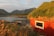 Smiling homeowner standing proudly in front of their newly finished rustic cabin by the sea in Homer, Alaska.