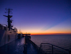 A merchant ship at sea with crew members preparing equipment on deck during sunrise.