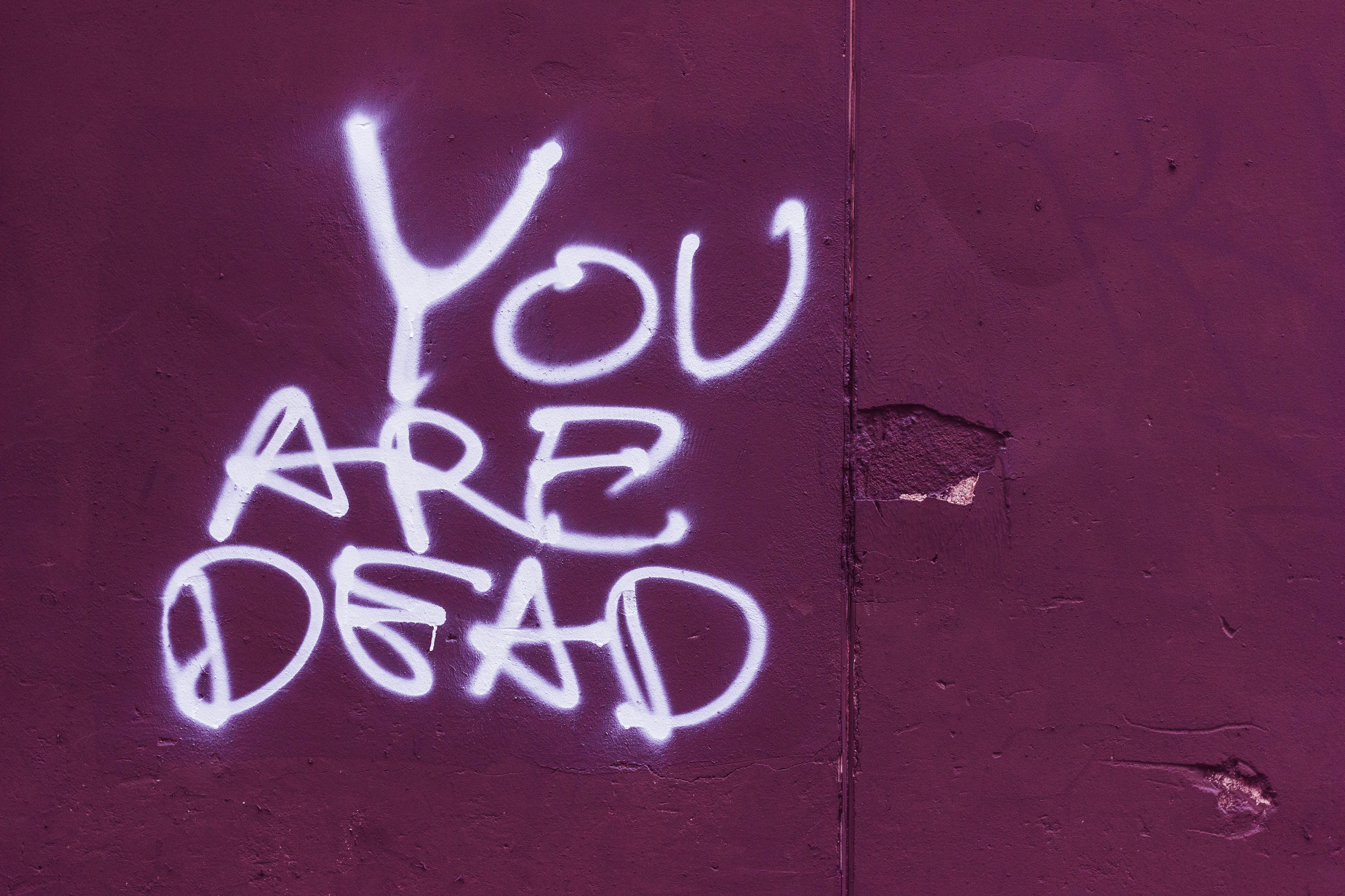 Hand written words spray painted on a plum coloured wall saying "You Are Dead".