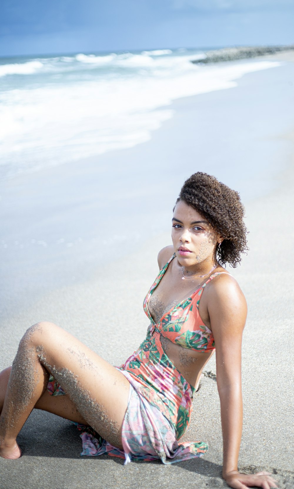 모래 위에 앉아있는 꽃무늬 수영복을 입은 여자