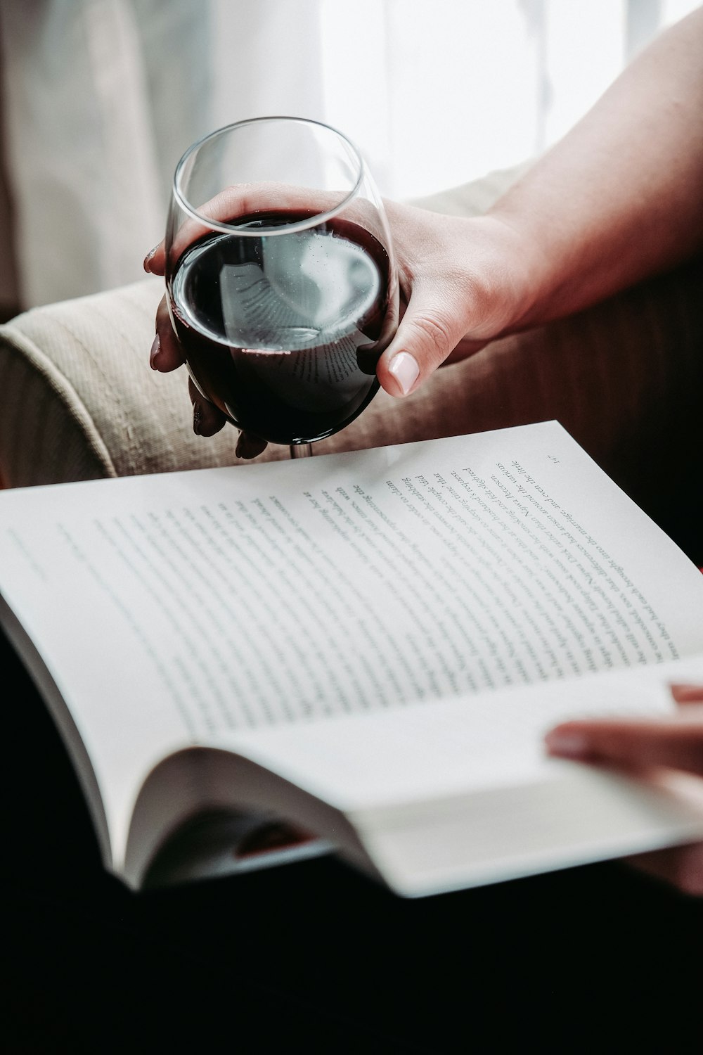 person holding goblet glass while holding book and reading