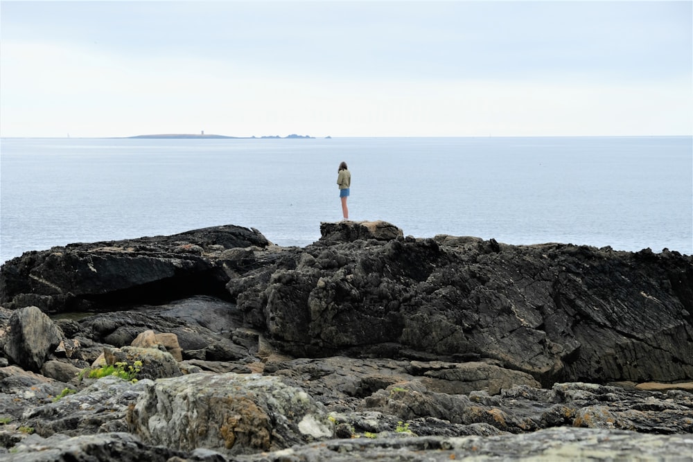 woman standing on cliff looking at sea during daytime