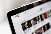 A close-up view of a computer screen displaying a YouTube page, showing the logo and multiple video thumbnails in a recommended section.
