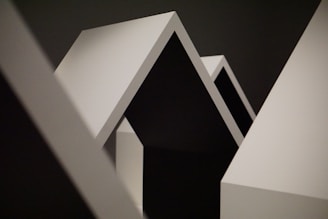 Geometric shapes with sharp angles and clean lines dominate the composition. The contrast between light and shadow highlights the minimalist design, featuring a series of triangular and rectangular forms.