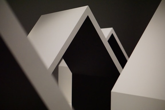 Geometric shapes with sharp angles and clean lines dominate the composition. The contrast between light and shadow highlights the minimalist design, featuring a series of triangular and rectangular forms.