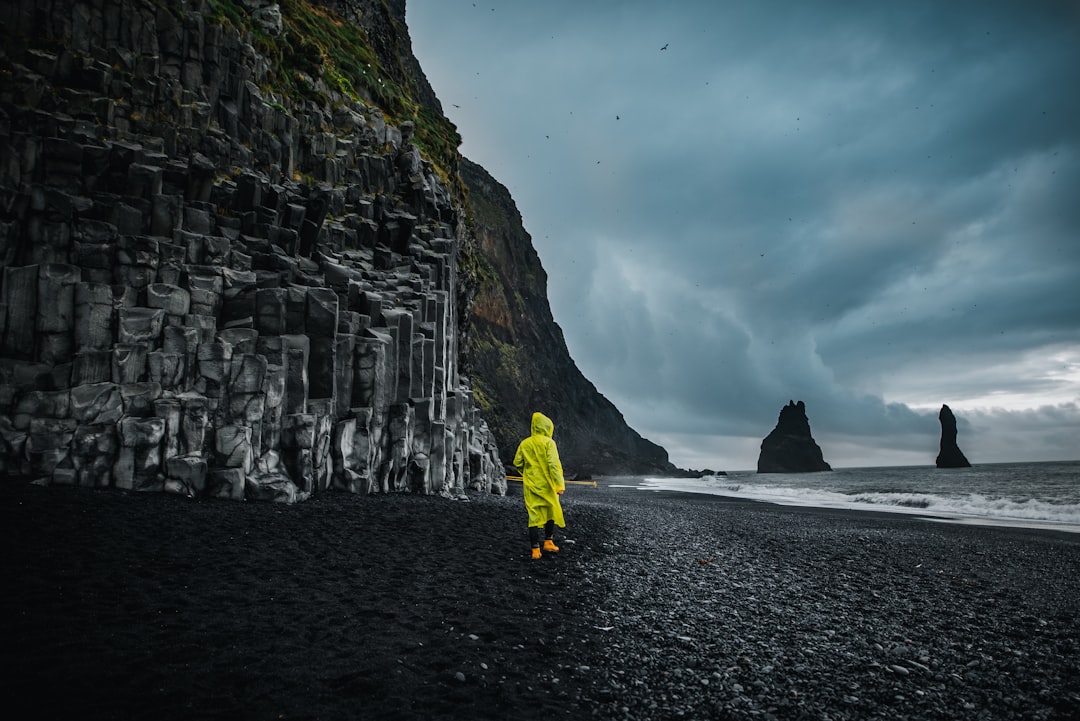 person wearing yellow rain coat standing on seashore