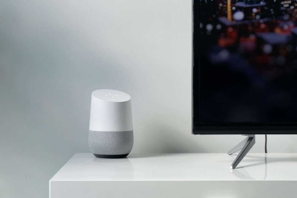 alto-falante inteligente do Google branco e cinza ao lado da TV de tela plana preta