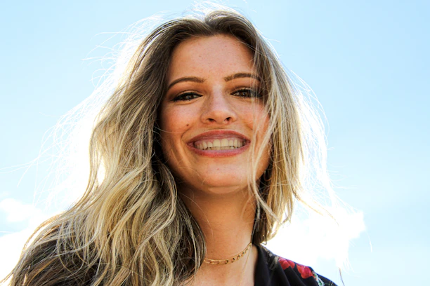 Smiling young woman wearing a bright ribbon clip in her hair, outdoors on a sunny day.