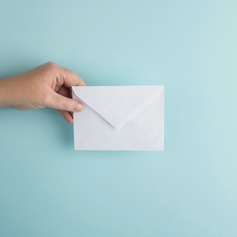 Hand holding a white envelope on a light blue background