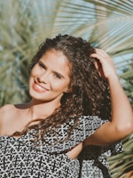 Close-up of a smiling woman gently touching her shiny, healthy curls outdoors.