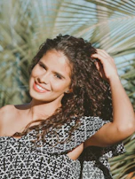 A woman smiling confidently with voluminous, glossy curls flowing in the breeze.