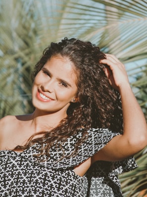 Close-up of a smiling woman gently touching her shiny, healthy curls outdoors.